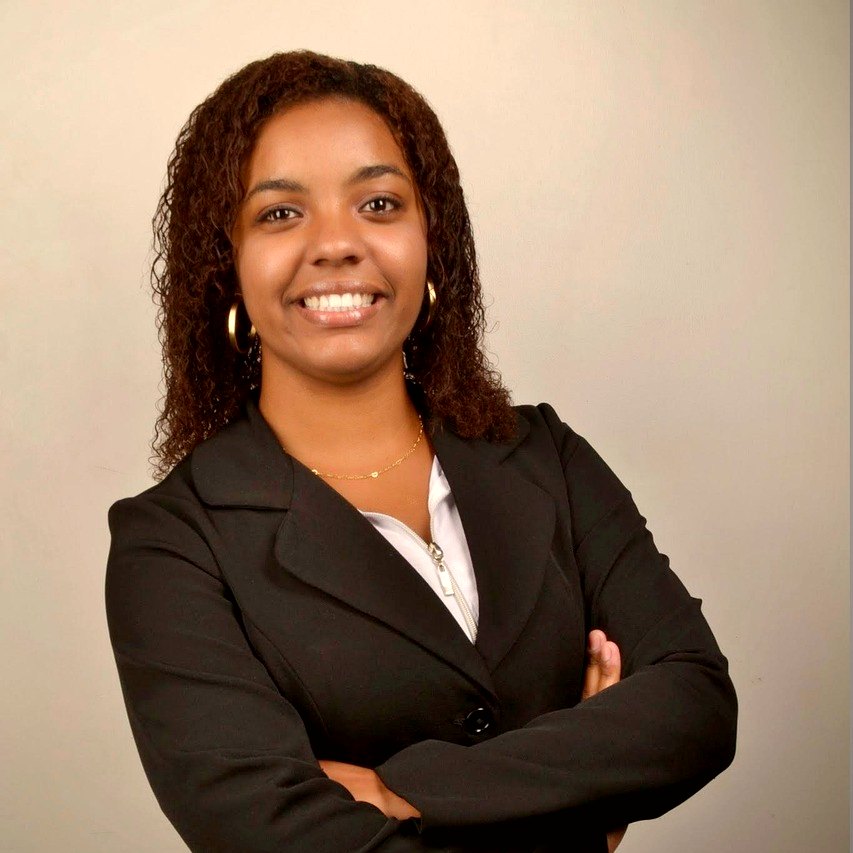 Mulher negra sorrindo, de terno, braços cruzados